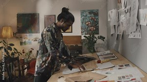 Eccentric Indian fashion designer crumpling pieces of paper while making sketching working on new collection in messy retro style atelier