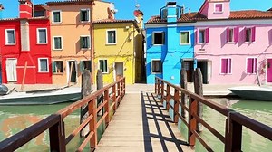 Colorful architecture in Burano island, Venice, Italy. Walking on the bridge over canal with boats. Red, pink, yellow and blue painted houses. Famous travel destination