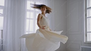 Woman dancer in fluttering dress whirls rapidly in expressive dance. Ballerina in white dress spinning in dance hall