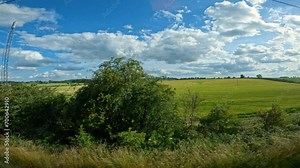 POV: View from the train window during a relaxing ride through green countryside. Beautiful sunny day for travelling by train past agricultural fields and meadows, with villages appearing between them