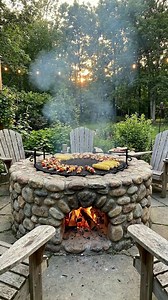 Where Firelight Meets Forest: The Timeless Joy of Outdoor Gatherings As the sun dips behind a curtain of tall trees, a soft golden glow settles over the garden. At the center of it all stands a beautifully crafted stone fire pit—solid, inviting, and alive with crackling flames. It’s more than a source of warmth; it’s the heart of the gathering. Food sizzles gently on the iron grill above the fire. Skewers of colorful vegetables and meats slowly roast, while golden ears of corn absorb the smoky a