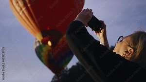 The girl looks at the sky where balloons are floating and films the process on her phone. Cool entertainment in the evening in the mountains Stock Video