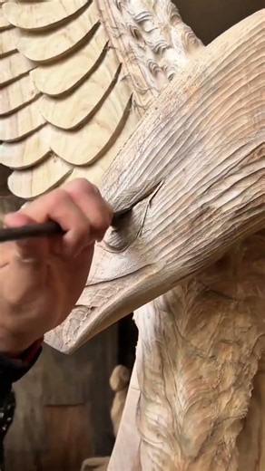 Worker Creating Intricate Feather Details on Wooden Sculpture