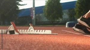 Sideways view male Caucasian professional athlete preparing beyond start line in a starting block and running, handheld shot.