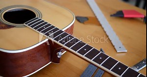 Close up hands of a luthier craftsman measuring an acoustic guitar neck fretboard on a wood workshop bench with lutherie tools.