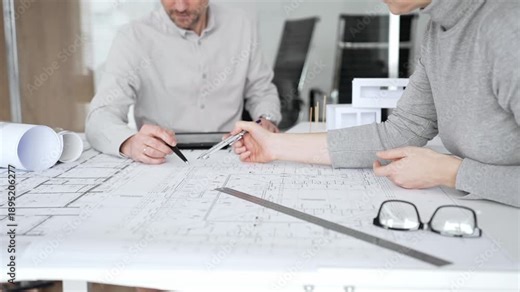 Architects are teamwork planning a building design project, reviewing detailed blueprints with a compass and a ruler, working on technical drawings and a digital tablet at the office, close up