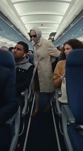 The Last Woman to Board Made the Entire Cabin Dead Silent. Passengers groaned as the aisle clogged again. “Unbelievable,” someone muttered, checking their watch. She stepped onto the plane slowly, one hand on the seatbacks for balance. Her coat was plain. Her shoes worn. No one looked twice—until they did. A flight attendant froze mid-smile. A businessman lowered his phone. The pilot, visible through the cockpit door, stood up. The woman removed her sunglasses. Every whisper stopped. To be conti