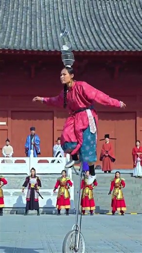 A woman rides a unicycle while skillfully kicking three bowls with her feet.