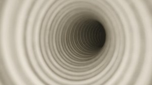 Close-up view down a coiled tube with a repetitive spiral pattern, creating a tunnel-like effect, emphasizing depth and symmetry in a soft, neutral tone
