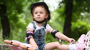 girl sits with rollers on curb of walkway and play the ball