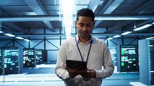 System administrator in data center managing and maintaining databases, ensuring data integrity, security and availability. IT worker updating server room supercomputers systems, camera B