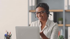 A dedicated African American woman teaches students online, utilizing a laptop and headset while creating an interactive and engaging learning environment from her home office.