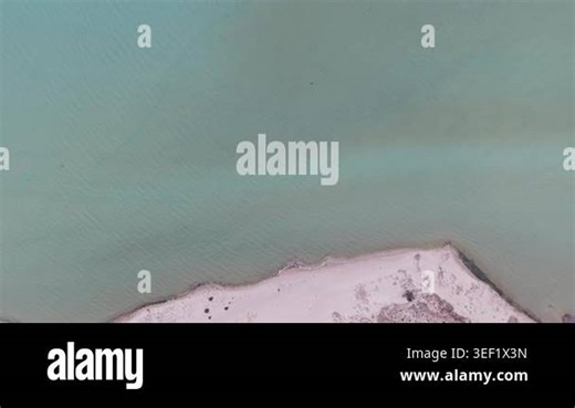 Aerial view of turquoise water meeting a pale sandy shoreline with subtle waves and minimal coastal vegetation Stock Video Footage - Alamy
