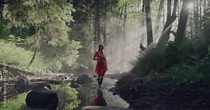 Enchanted Forest Stroll: A woman in a vibrant red dress walking along a riverbed through a lush, fairy-tale like forest amid the mystical morning mist and fog.