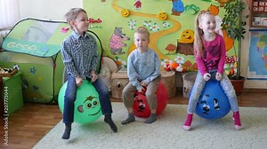 Children have fun sit and jump on large rubber inflatable balls in playroom