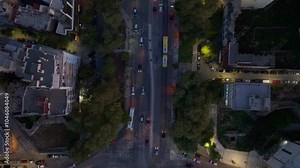 Bird's eye view of cars driving through an intersection in Thessaloniki, Greece. Buildings and streets are illuminated by lights as the sun sets
