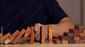 Man using finger or hand to prevent domino wooden blocks falling, finance or business strategy, risk protection. Risk assessment concept.