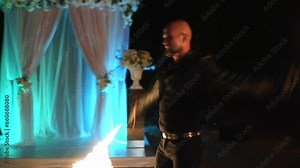 Male artist making a fire performance show with flame at festival at night. Artist juggling with burning fire fans near the hotel. Fire show performance with burning torch on the street.