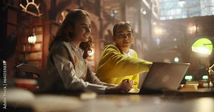Two Beautiful Girlfriends Studying in a College Library. Stylish Female Helping Her Classmate Colleague with Homework. Couple Using Laptop Computer for a Research and Exam Preparation