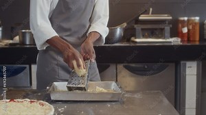 Tilt down shot of African American chef in apron grating cheese for dish cooking at kitchen of cafe