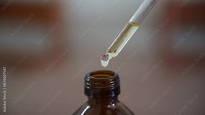 A female hand dripping from a pipette cosmetic liquid, serum above the brown glass bottle