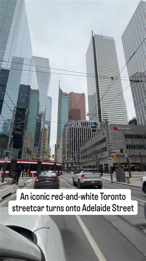 An iconic red-and-white Toronto streetcar turns onto Adelaide Street, with Toronto’s skyline beyond