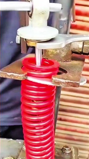 "Red coil spring compressed, metal press tests precise resilience."
