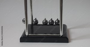 Selective focus on chromatic spheres wobbling and slowing down. Newton's cradle. Kinetic pendulum. Inertia as physical phenomena. Physics lesson. Newton's balls swinging against white background