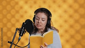 Narrator wearing headset reading aloud from book into mic against yellow background. Upbeat professional voice actor recording audiobook, creating engaging media content for listeners, camera A