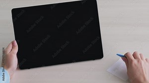 Online consultation. Web conference. Remote job. Female hands holding pen paper note on table with portable computer blank screen copy space.