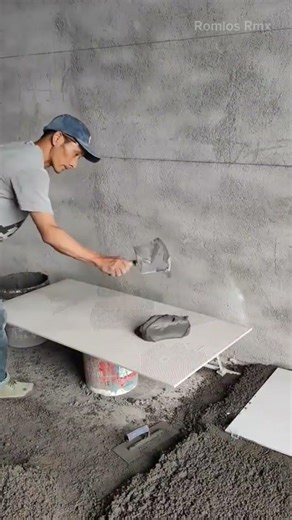 installing many large white ceramic floor tiles using fresh wet cement on the construction site