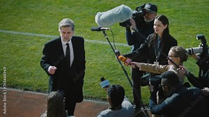 SEO or director of soccer team answering press questions and giving interview near football field before match. Private investor crowded by news journalists. Inspirational speech on press conference.