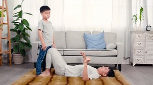 4K, Dad slept on carpet, covering the floor, raised legs, making son sit on legs, raised legs when son sat down make pattern come up, boy and father put hands together, balancing on his father's legs.