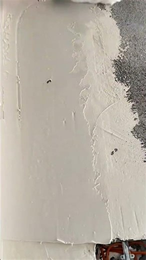 applying a smooth layer of white plaster over a grey textured wall using a metal finishing trowel