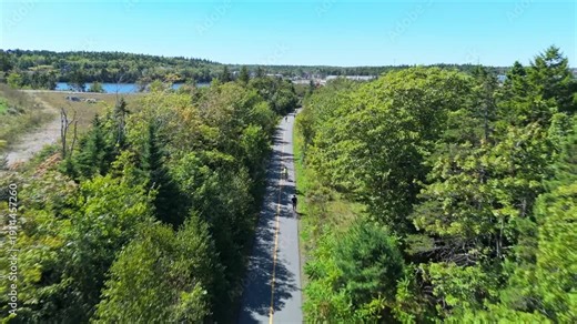 Drone footage shows a helmeted man cycling through Halifax park. Summer greenery, open space, smooth asphalt and vitality reflect outdoor freedom and wellness in Nova Scotia capital.