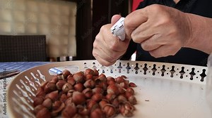 old man hand cracks walnuts with nutcracker. Broken hazelnut shells. Pieces of shell fruits.