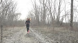 Woman running in autumn winter cardio exercise - woman jogging doing her workout outside. Young adult running in outdoor park with forest background wearing cold weather gear.