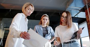 Team of young beautiful women standing over the table and discussing project. IT employees. Successful females talking and brainstorming. Startup concept. Meeting with colleagues.