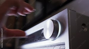View of the control panel on music center. Tumblers, knobs and buttons. Female hand turn on and increasing music volume. Close up view.