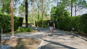 Young man jogging along serene park path surrounded by lush greenery, engaging in morning fitness routine for personal well-being and health. Outdoor exercise and recreational activity.