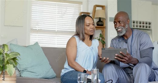 Mature couple on sofa, man in scrubs turning tablet, tapping, checking results with stethoscope