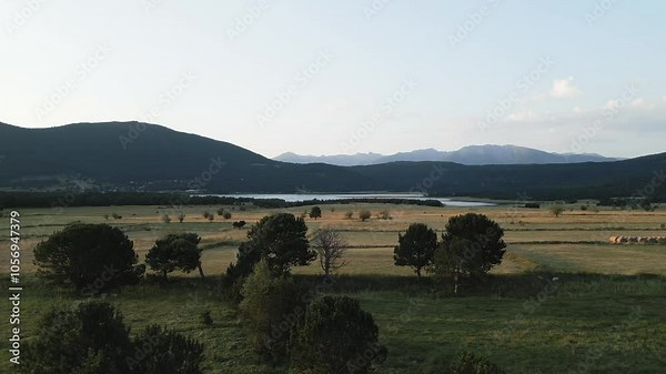 Camera pans across a wide shot of the lac de matemale in the pyrenees mountains, revealing a serene landscape of forests, fields, and distant peaks