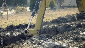 Big excavator is digging foundations of house. Excavating of hole. Construction machinery, ground works. Yellow digger works on building. Static day stabilized v-log shot. Bucket digs in clay.