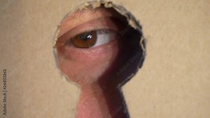 curious human eye looks into the hole in the form of a keyhole.hole in the cardboard wall.extreme close-up.shallow depth of field.