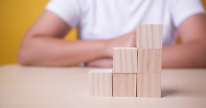 clip-1098259321-hand-putting-wood-cube-on-top-block