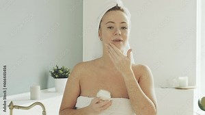 Portrait of woman wrapped in towel in bathroom. female, after waking up and taking shower, takes moisturizing cream from jar and is applied to face and rubs it into skin to give softness.