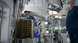 Medicine infusion pump machine and lung ventilator pump working in surgery room. Medics in uniforms are at backdrop in blur.