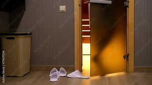 Man in white bathrobe entering dry sauna to warming, legs close-up, rear view. Healthy recreation, wellness concept. Body care in steaming room, heating procedure, treatment, traditional leisure.