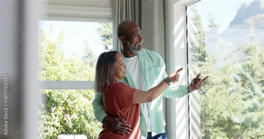Mature couple at window, woman with smartwatch spotting view to observe and pointing, man gesturing