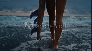 Legs close up, a female surfer with a surfboard, walking along a sandy beach or coast. Feet of a beautiful girl goes surfing in Bali. Surfer female holds a board for the sea, goes into the water, wave